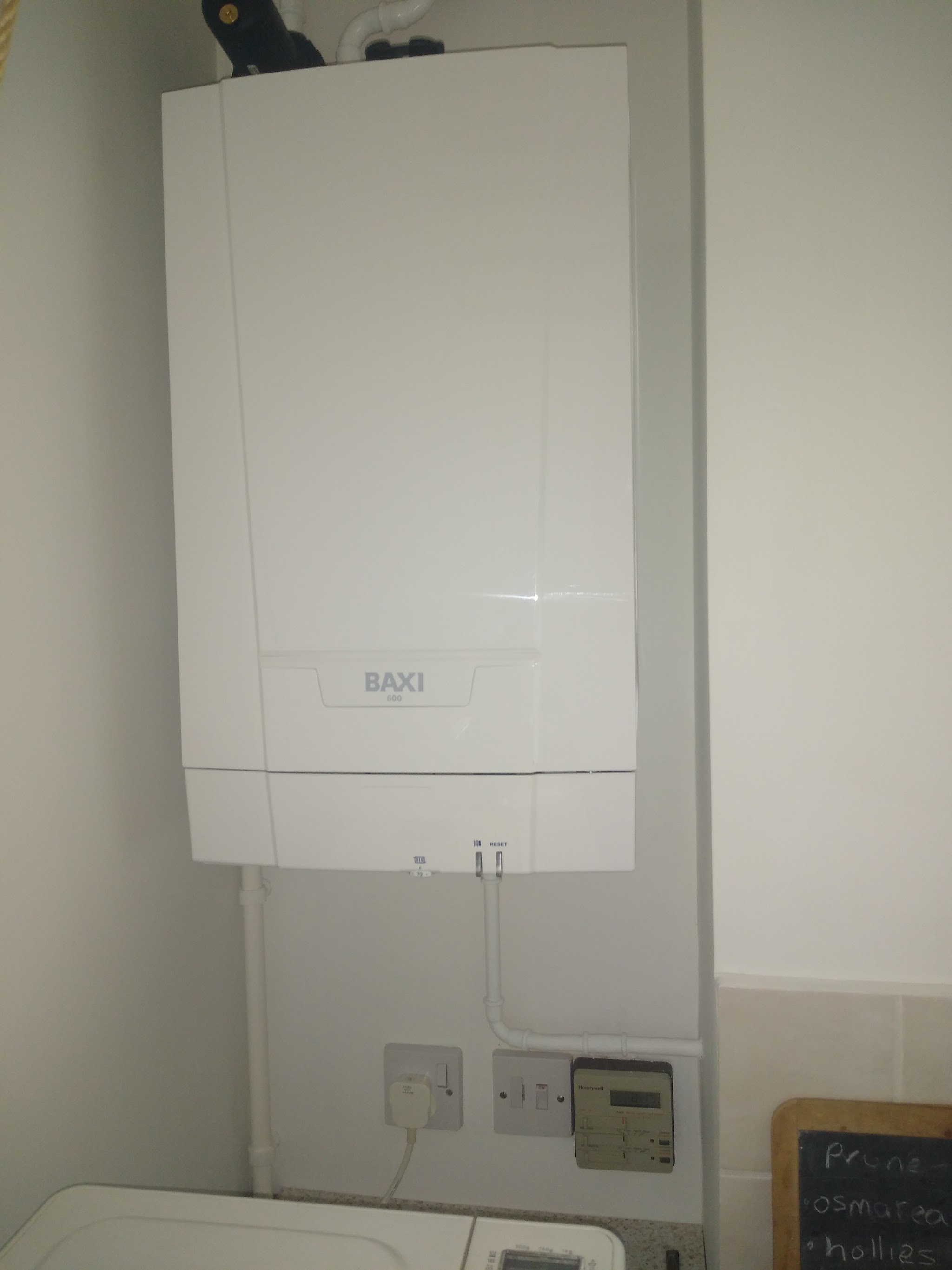 A newly fitted white Baxi combi boiler on a utility room wall, with its programmer below